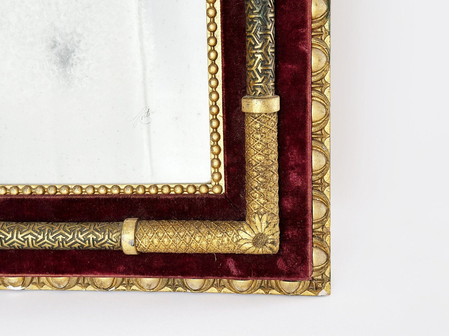 Bottom corner of ornate Victorian frame with another view of the flower detail of the corner. The gold accents of the frame are accentuated by the placement over a rich red velvet.