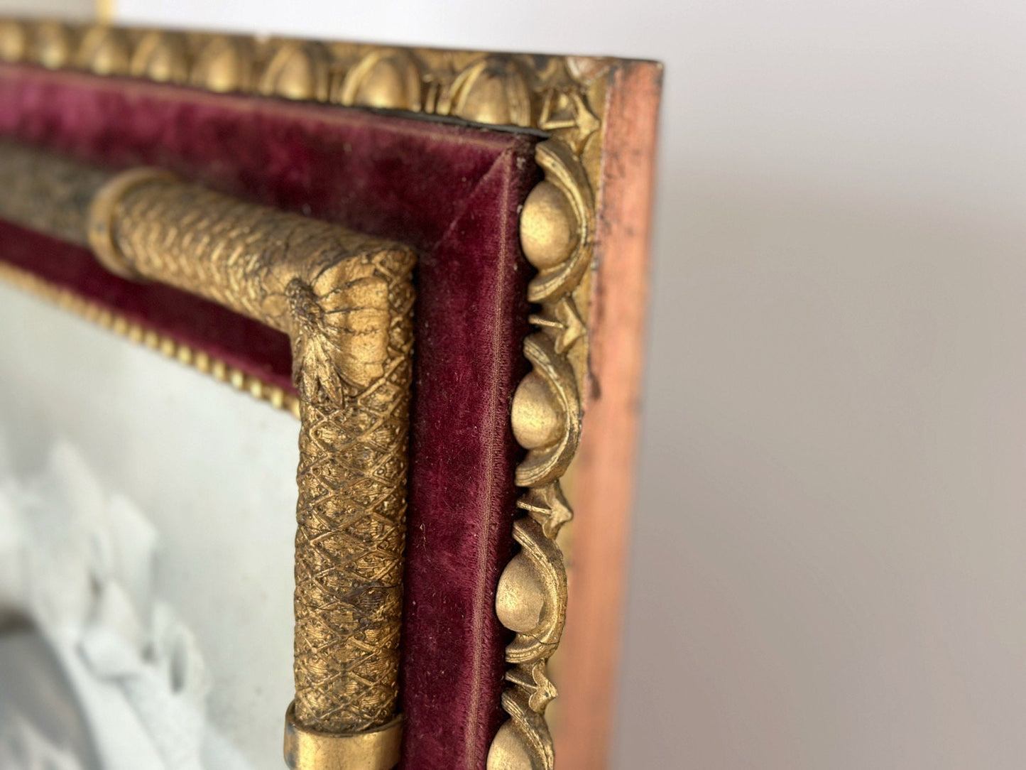 A close up view of the side edge of this stunning ornate antique frame show a copper finish on the outside. You can see how the gold finish on this Victorian frame come to life next to the copper and red velvet.