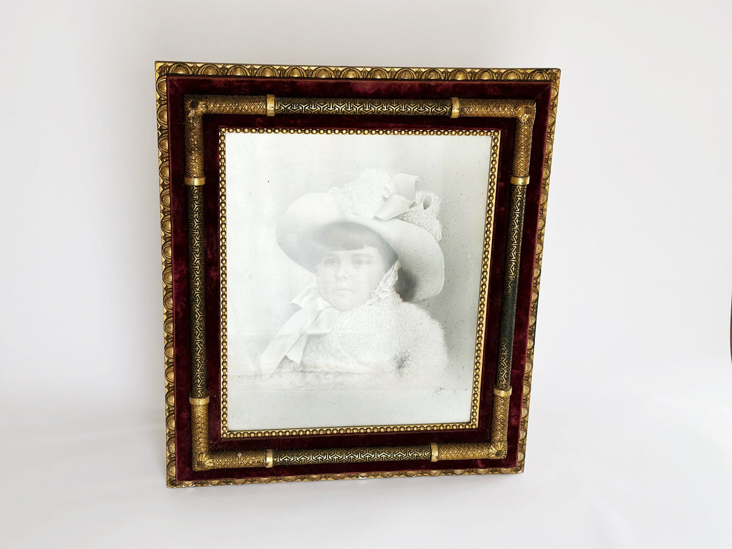 A full look at the large antique Victorian frame. This is a blend of the eras, likely late Art Nouveau and early Art Deco given the patterns and design features of the frame. The frame still holds the original portrait of a young child.