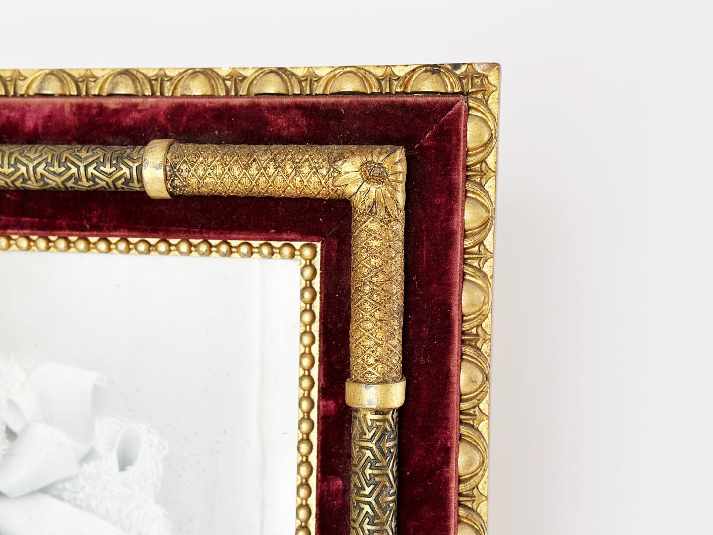 Top right corner of a rare unique antique Victorian era portrait frame featuring gold elements over red velvet. It shows a transition from Art Nouveau floral to Art Deco patterns.