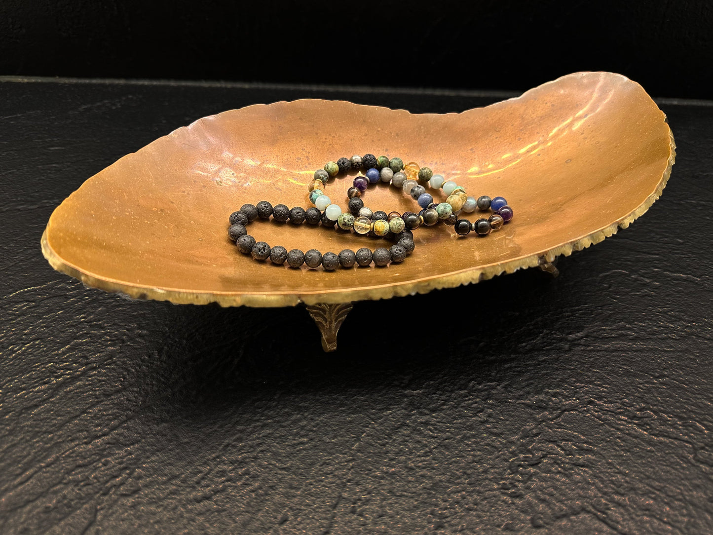 Copper Jewelry Tray with Bracelets in the center of the bowl. The tray is on a black counter which shows the ornate beauty.